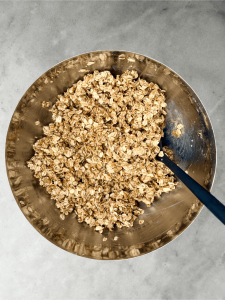 Rolled oats coated with almond butter mixture in a mixing bowl, ready to be baked into protein granola.