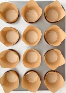 Overhead shot of a muffin tin lined with tall brown tulip liners, ready for baking high protein pumpkin breakfast muffins.