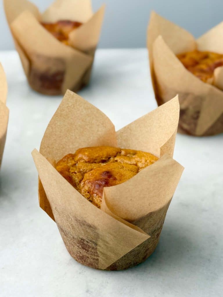 Close-up of a freshly baked high protein pumpkin muffin in a tall brown tulip liner on a marble surface.
