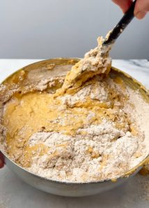 Smooth orange pumpkin batter made with protein powder and Greek yogurt being whisked in a stainless steel mixing bowl.