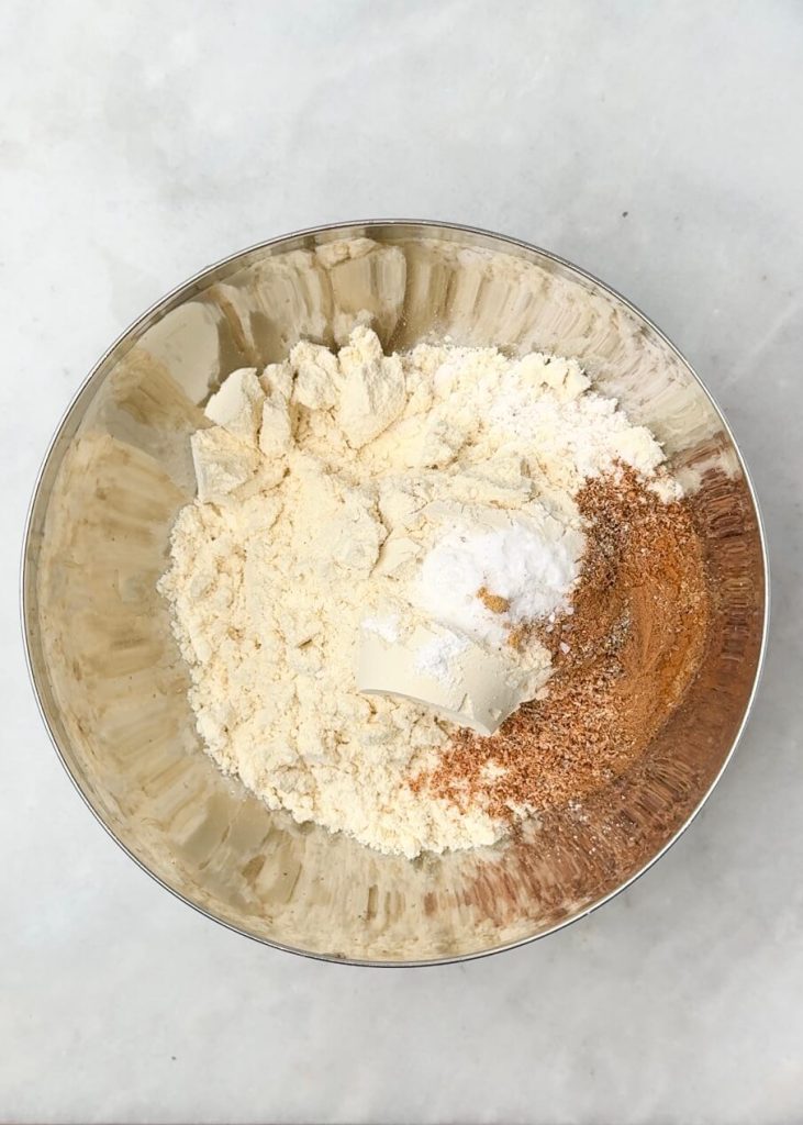Bowl of dry ingredients including protein powder, oat flour, baking powder, and pumpkin spice for high protein pumpkin oat muffins.
