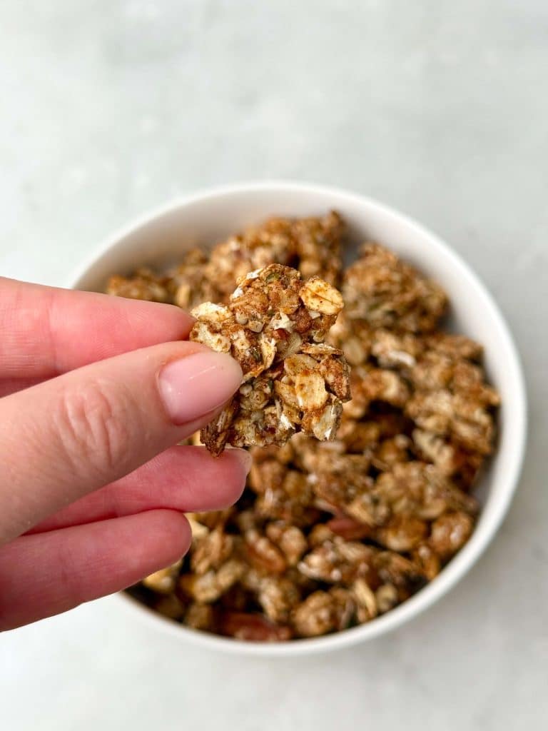 Hand holding a large crunchy cluster of homemade protein granola over a bowl filled with more granola.