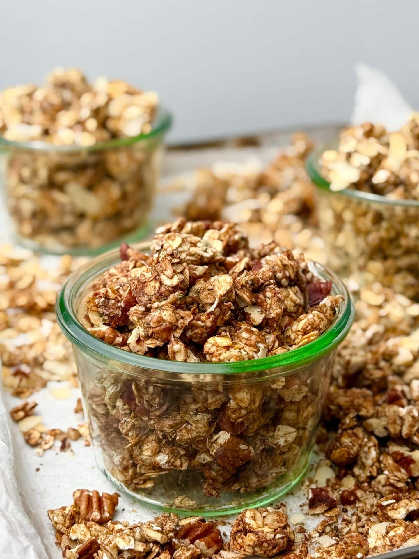 Glass jars filled with chunky homemade protein granola clusters on a baking sheet.