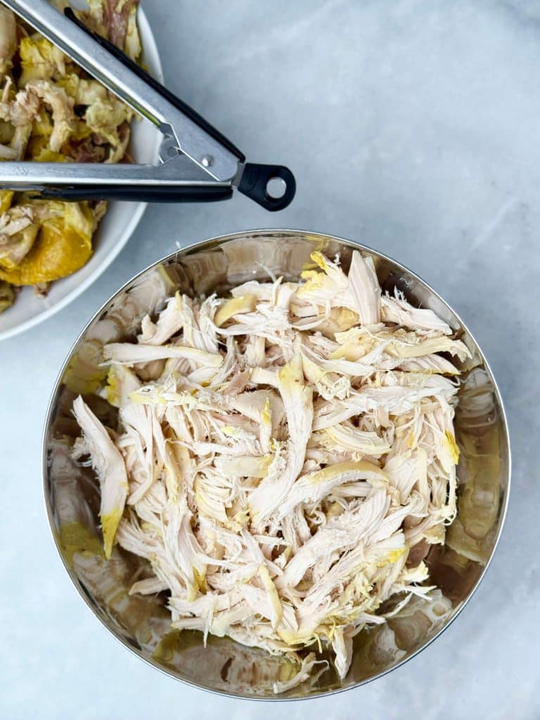 Bowl of freshly shredded chicken breast and thighs, ready to be added back into crockpot chicken noodle soup.