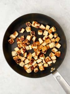 Golden fried halloumi cubes in a skillet, ready to be added to a high-protein fall lentil salad.