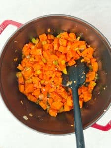 Cooked vegetables including carrots and celery sautéing in a pot with tomato paste as the base for healthy lentil soup.
