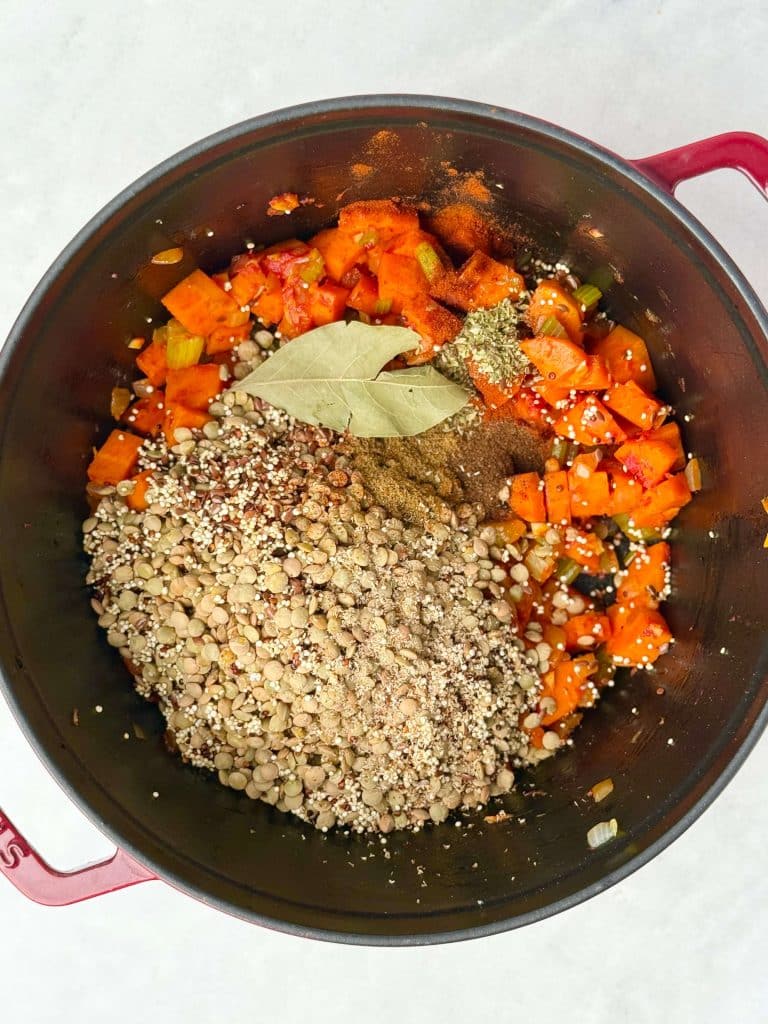 Dry lentils, quinoa, flax seeds, bay leaf, and spices added to sautéed vegetables in a pot before simmering into vegan lentil soup.