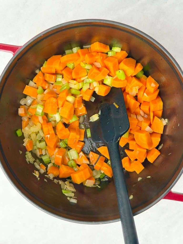 Diced carrots, celery, and onions sautéing in a Dutch oven as the base for homemade vegan lentil soup.