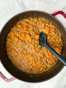 Thick and cozy lentil soup with quinoa and vegetables in a pot, showing carrots, celery, and spinach in a tomato-based broth.