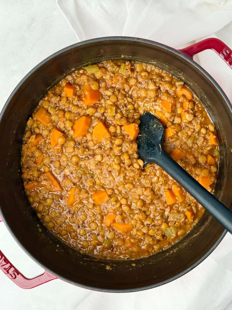 Thick and cozy lentil soup with quinoa and vegetables in a pot, showing carrots, celery, and spinach in a tomato-based broth.