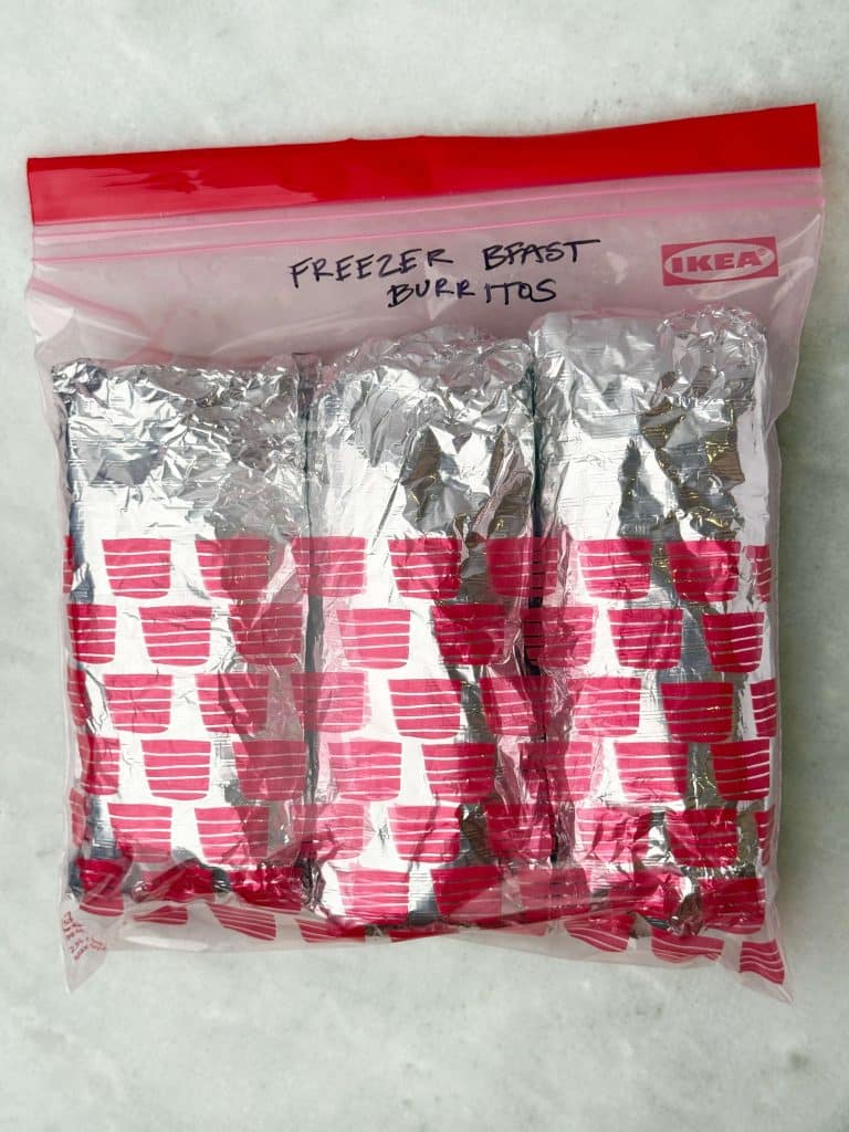 Foil-wrapped high protein freezer breakfast burritos stored in a labeled zip-lock bag for easy make-ahead meal prep.