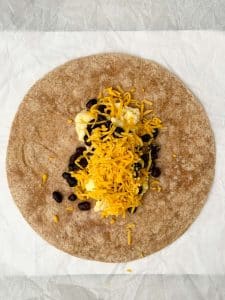 Whole wheat tortilla filled with scrambled eggs, black beans, and shredded cheddar cheese for a high protein freezer breakfast burrito.