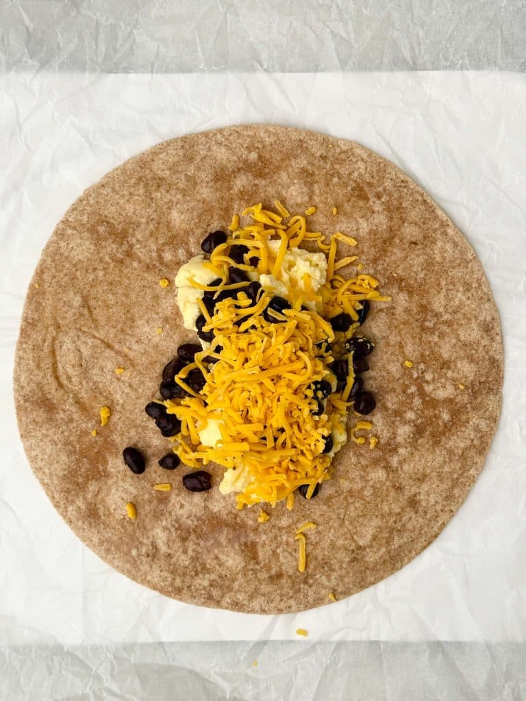 Whole wheat tortilla filled with scrambled eggs, black beans, and shredded cheddar cheese for a high protein freezer breakfast burrito.