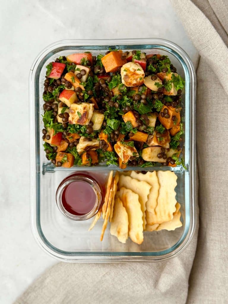 Fall lentil salad packed into a glass meal prep container with dressing on the side for easy high-protein lunches.
