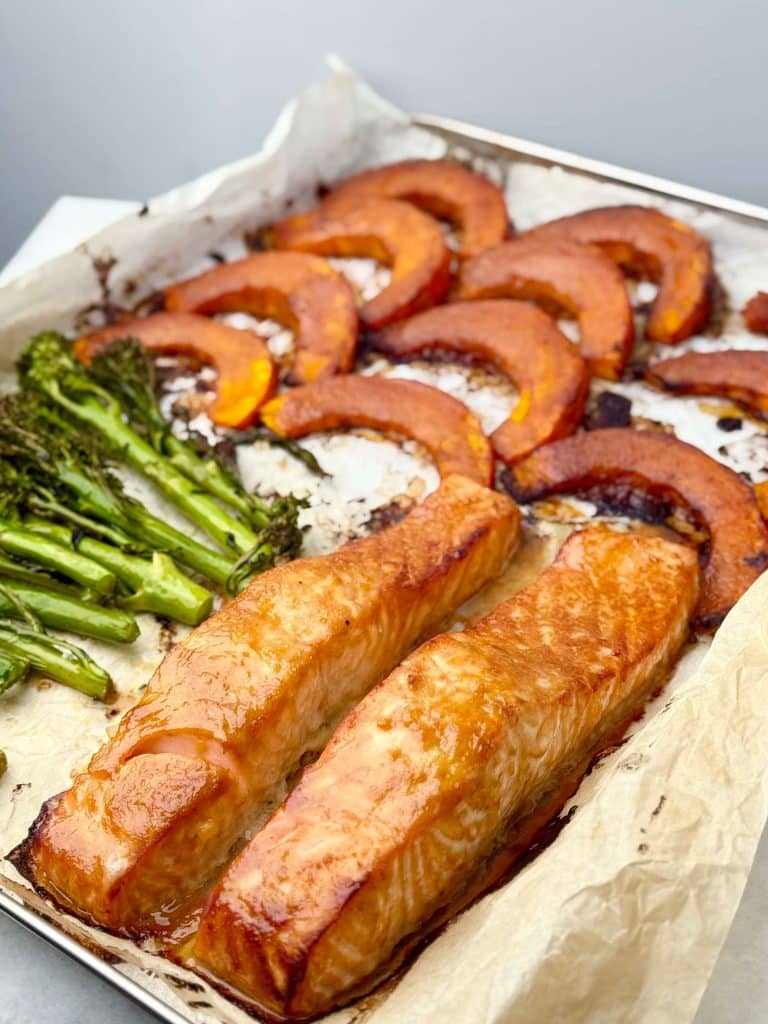 Half-roasted kabocha squash on a sheet pan with fresh broccolini and miso-marinated salmon filets
