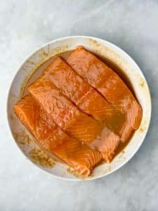 Raw salmon filets marinating in maple miso sauce in a shallow white bowl