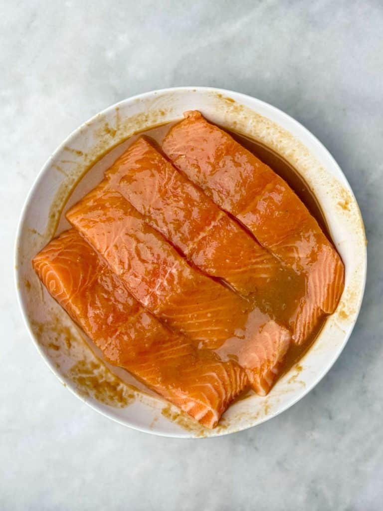 Raw salmon filets marinating in maple miso sauce in a shallow white bowl