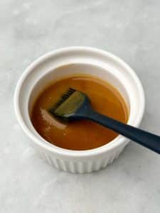 Glossy miso butter sauce in a small white ramekin with a black silicone brush