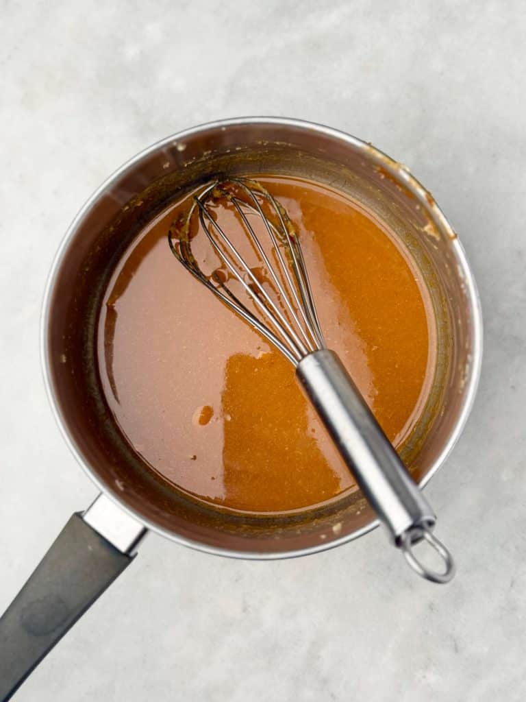 Silky maple miso marinade simmering in a saucepan with a whisk on a white background