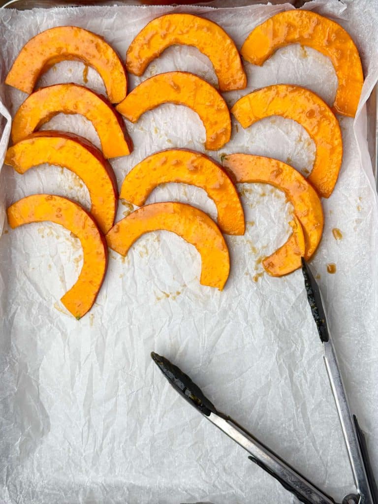 Thin slices of kabocha squash tossed in miso marinade, arranged on a parchment-lined sheet pan