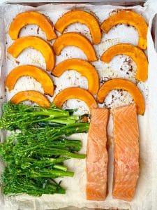 Sheet pan with raw salmon, broccolini, and marinated squash, ready to go in the oven