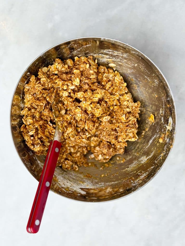 Pumpkin spice protein ball mixture in a stainless steel bowl with a red-handled spoon.