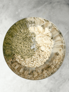Dry ingredients including rolled oats, hemp hearts, protein powder, and sea salt in a mixing bowl for homemade protein granola.