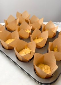 Muffin tin filled with tall tulip liners, each half-filled with pumpkin muffin batter before baking.