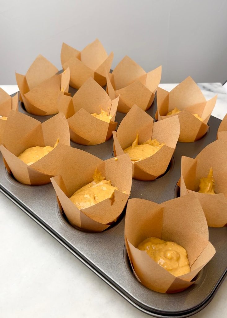 Muffin tin filled with tall tulip liners, each half-filled with pumpkin muffin batter before baking.