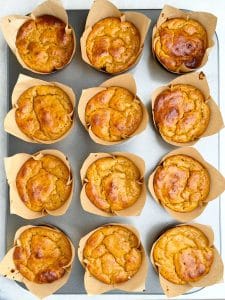 Freshly baked high protein pumpkin muffins in brown tulip liners cooling in the muffin tin with golden, slightly cracked tops.