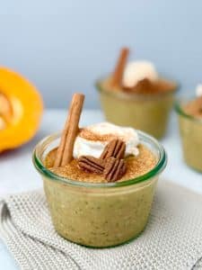 Close-up of pumpkin overnight oats in a glass jar, garnished with greek yogurt, pecans, and a cinnamon stick for a cozy fall presentation.