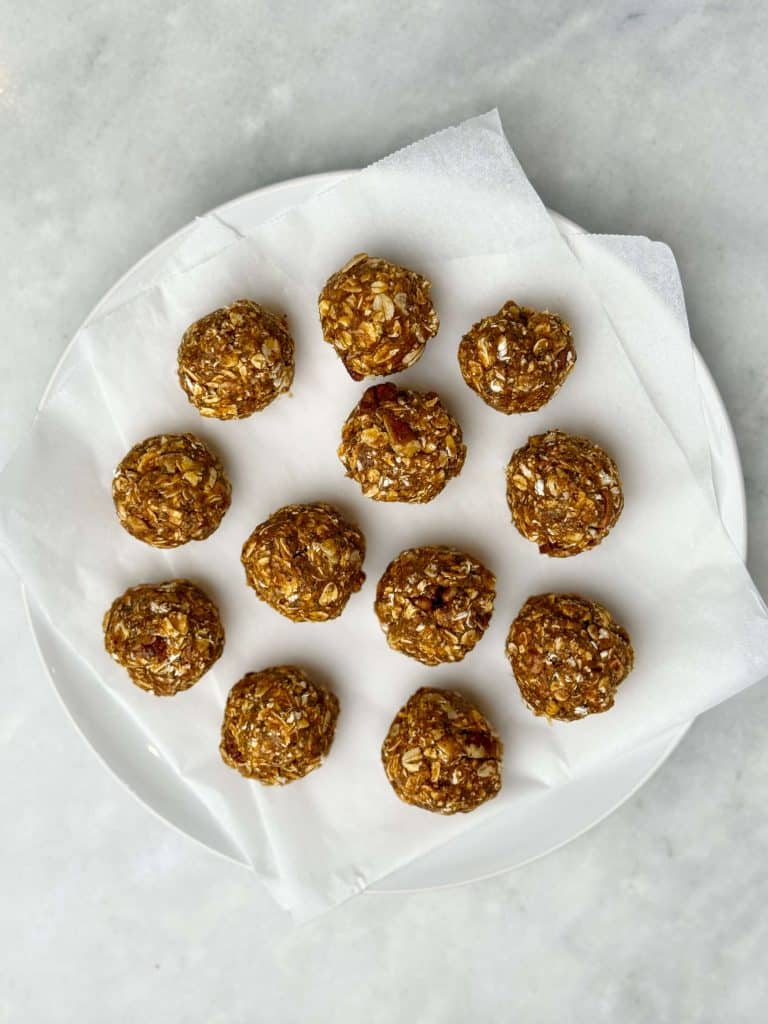 Pumpkin spice protein balls arranged on a white plate lined with parchment paper, ready to chill.