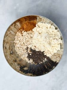 Dry ingredients for pumpkin spice protein balls — oats, protein powder, chia seeds, and pumpkin pie spice — in a mixing bowl.