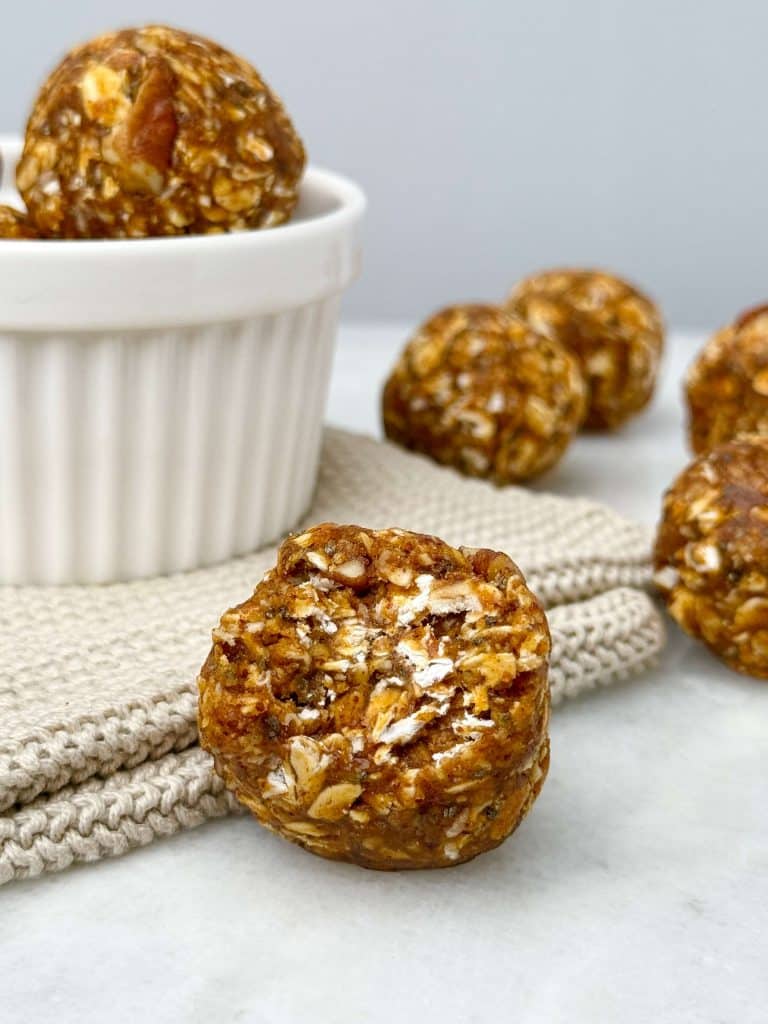 Pumpkin spice protein ball close-up in front of a white ramekin with more balls in the background.