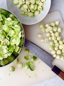 Fresh Brussels sprouts being trimmed and prepped on a cutting board with a chef’s knife.