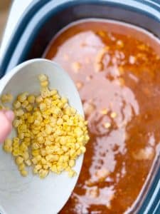 Slow cooker birria soup with corn being added into the red chili broth.