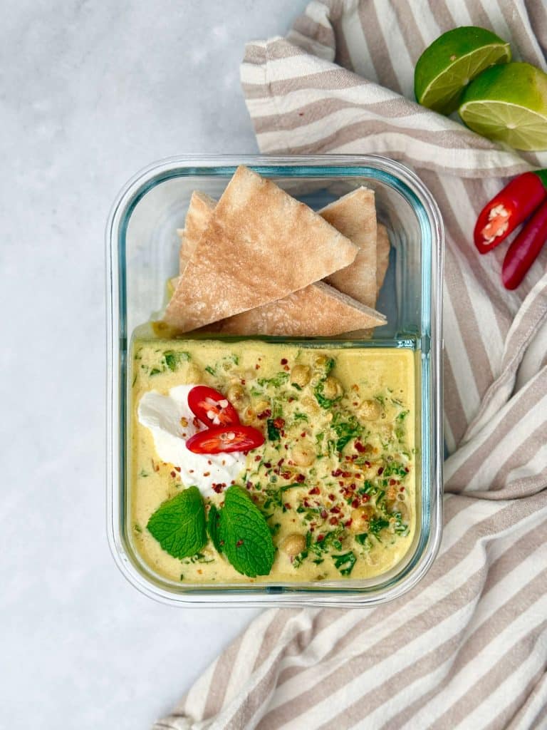 Glass meal prep container with spiced chickpea stew, pita wedges, yogurt, mint, and chili flakes.