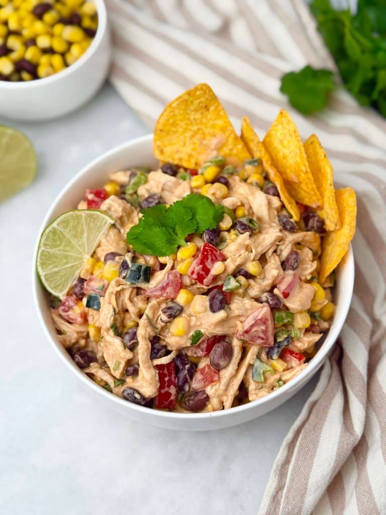 Overhead view of Southwest Chicken Salad in a white bowl with lime, cilantro, and tortilla chips for garnish.