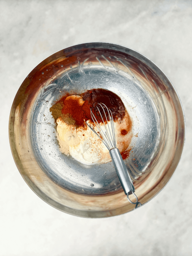 Bowl of creamy Southwest dressing made with Greek yogurt, mayonnaise, BBQ sauce, lime juice, and spices with a whisk.