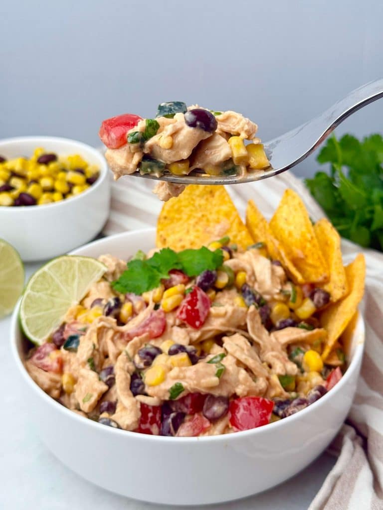 Forkful of Southwest Chicken Salad with chicken, corn, beans, and tomatoes held above a serving bowl.