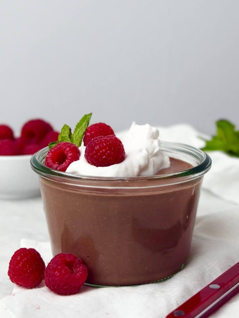 Glass jar filled with creamy chocolate protein pudding made from blended cottage cheese, topped with coconut yogurt, fresh raspberries, and a mint sprig.