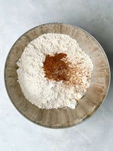 Dry ingredients in a mixing bowl with cinnamon and nutmeg for apple cinnamon muffins.