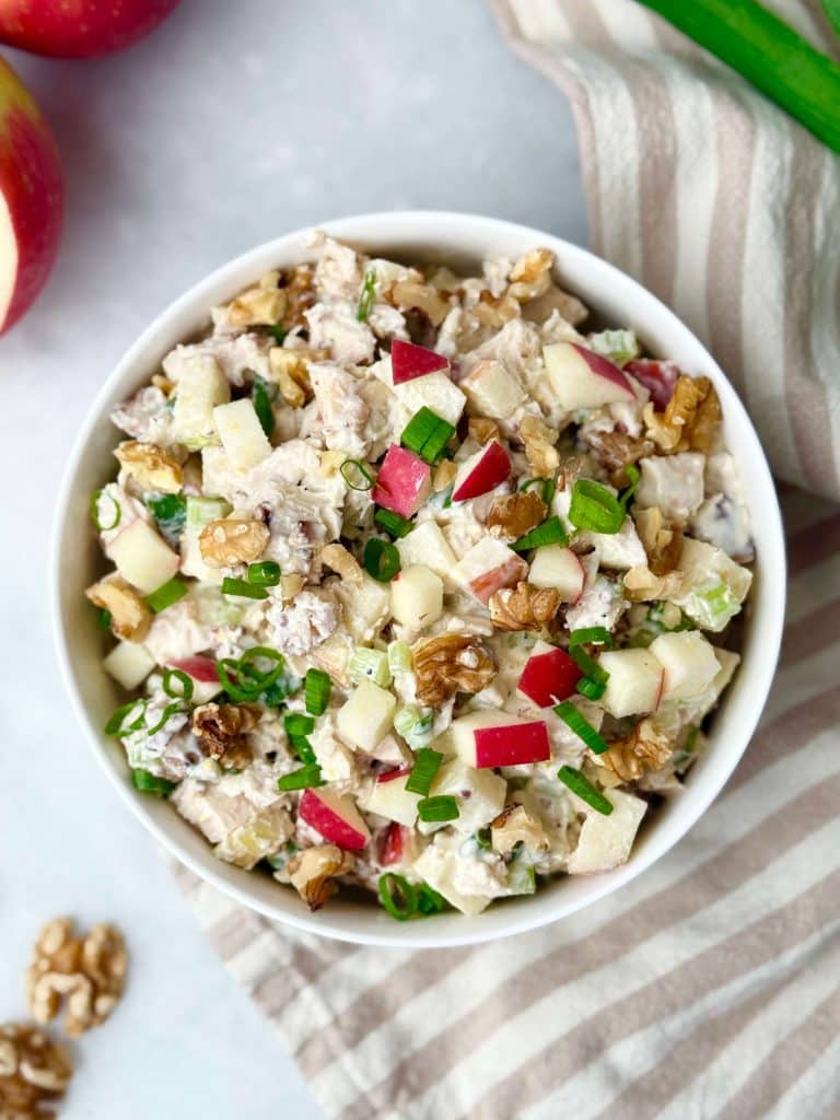 Overhead view of apple walnut chicken salad with diced apples, celery, walnuts, and scallions in a white bowl.