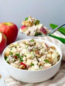 Spoonful of creamy apple walnut chicken salad with diced apples, walnuts, and green onions held above a bowl.