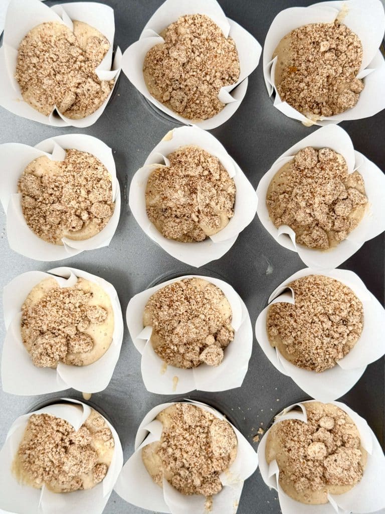 Unbaked apple cinnamon muffin batter in liners topped with cinnamon protein crumble before baking.
