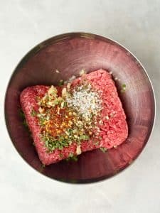 Ground beef mixed with herbs, garlic, and spices in a metal bowl for homemade beef breakfast sausage patties.