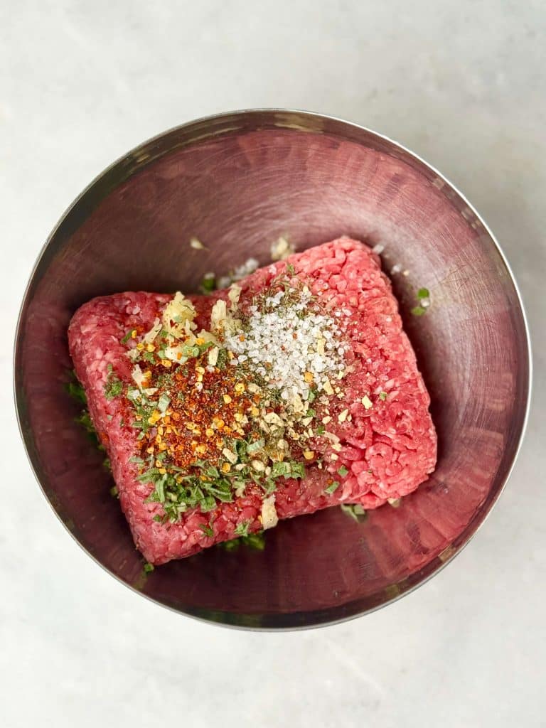 Ground beef mixed with herbs, garlic, and spices in a metal bowl for homemade beef breakfast sausage patties.