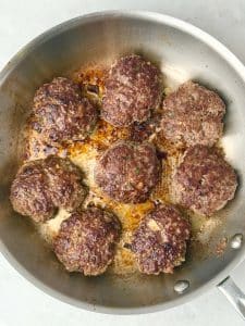 Homemade beef breakfast sausage patties sizzling in a stainless steel skillet, browned and juicy with herbs and spices.