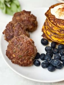 Plate with homemade beef breakfast sausage patties, pumpkin protein pancakes, and fresh blueberries.