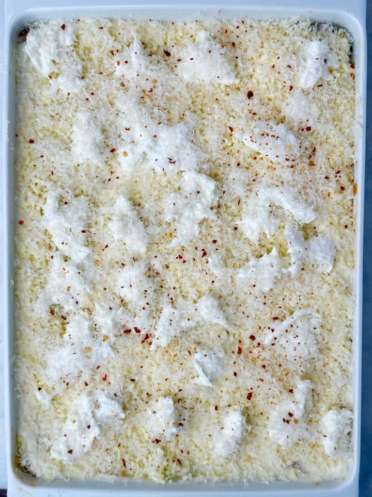 Unbaked lasagna topped with torn fresh mozzarella, grated Parmesan, and red pepper flakes before going into the oven.